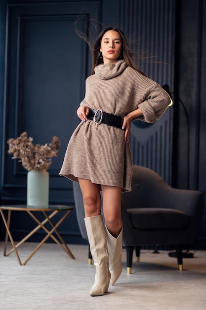 Young beautiful brunette woman in beige boots in a beautiful interior Full length portrait Young elegant woman wearing beige stylish look Pretty girl with long brunette wavy hair Fashionable lady