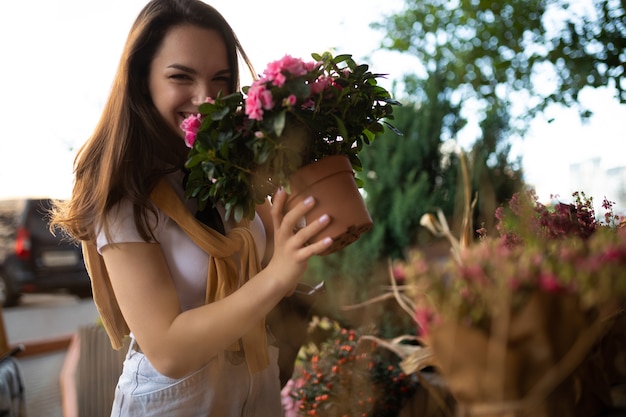 Giovane bella donna castana che gode dei fiori in vaso sul portico di un negozio di fiori