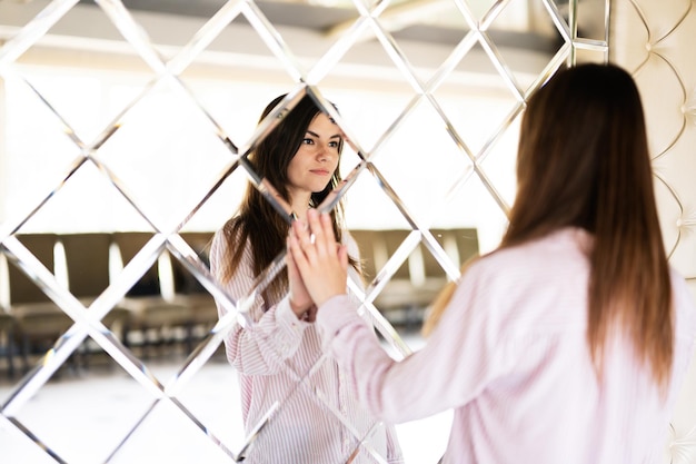 Giovane bella donna castana in camicia che tocca specchio fatto di rombi