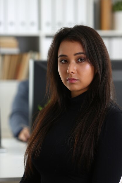 Young beautiful brunette woman sit at table in office in cabinet of her boss