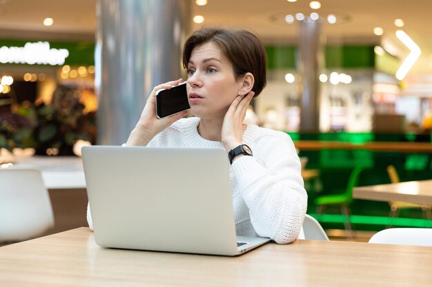 Young beautiful brunette woman sitting at a shopping center at a table and working at a computer