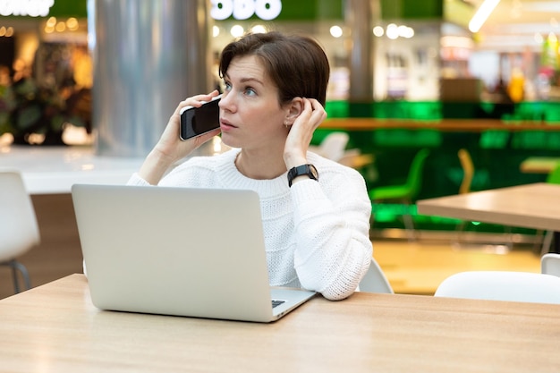 Young beautiful brunette woman sitting at a shopping center at a table and working at a computer