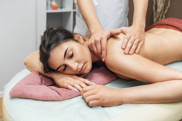 Молодая красивая брюнетка женщина в спа-салоне отдыхает во время сеанса массажа трапециевидных мышц и шейного отдела