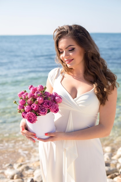 Young beautiful brunette woman in white dress walking near the sea
