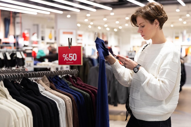 Young beautiful brunette woman with a short haircut in a white sweater chooses stylish clothes in a store in a shopping mall