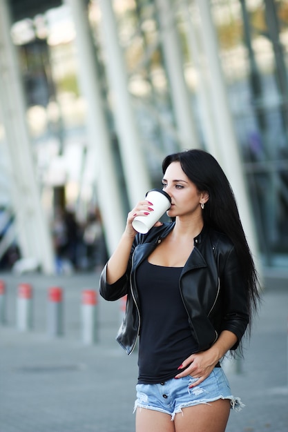 Young beautiful business woman drinks coffee near beside office building