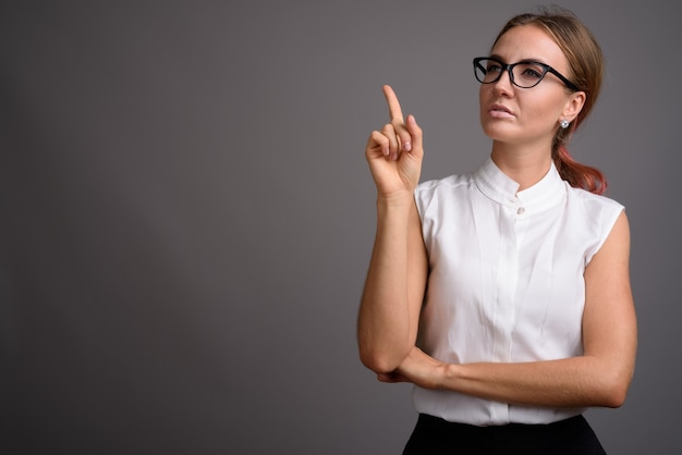 Young beautiful businesswoman against gray wall