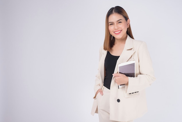 Young beautiful businesswoman in suit holding tablet over white Studio background