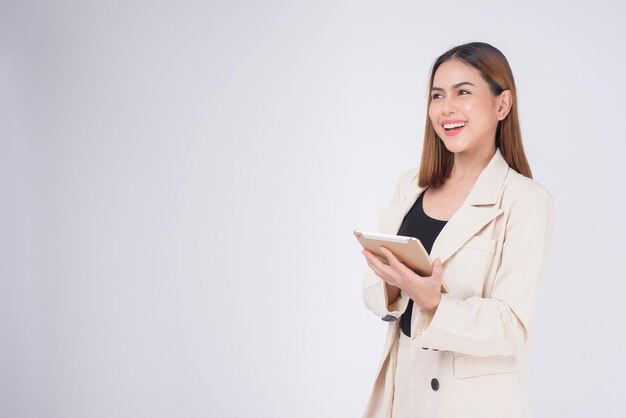 Young beautiful businesswoman in suit holding tablet over white Studio background