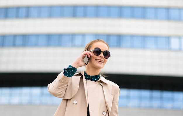 サングラス、電話、ラップトップ、街の通りでのコーヒーのカップを持つ若い美しい女性実業家