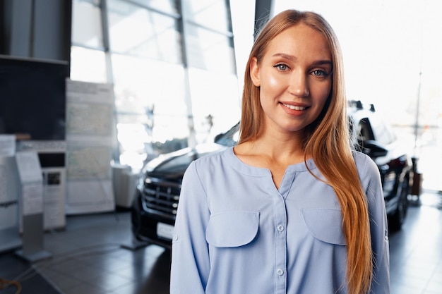 車のショールームに立っている若い美しい車のセールスウーマン