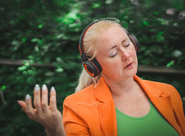 Young beautiful caucasian blonde woman listens to music with closed eyes sits in an outdoor cafe