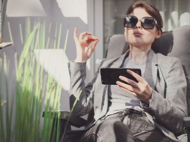 Young beautiful caucasian girl sitting in a garden chair in the backyard and meditating online