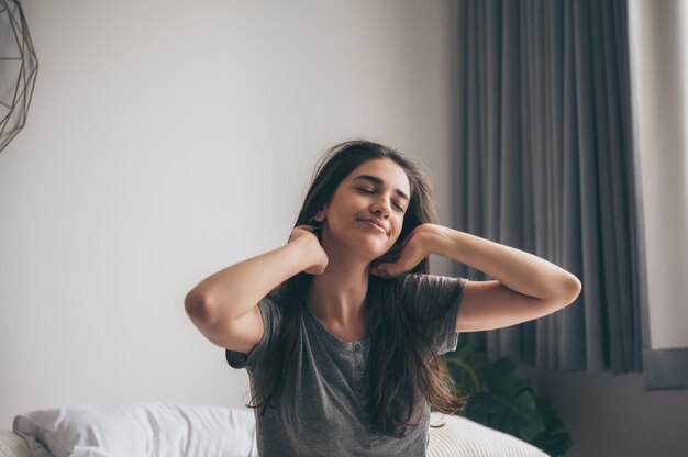 A young beautiful caucasian long brown hair women enjoy the moment on bed in the morning, smiling girl stretching on the bed, morning person, ralaxing on the bed.