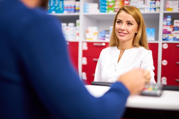 Young beautiful caucasian pharmacist is working with customer in modern drugstore