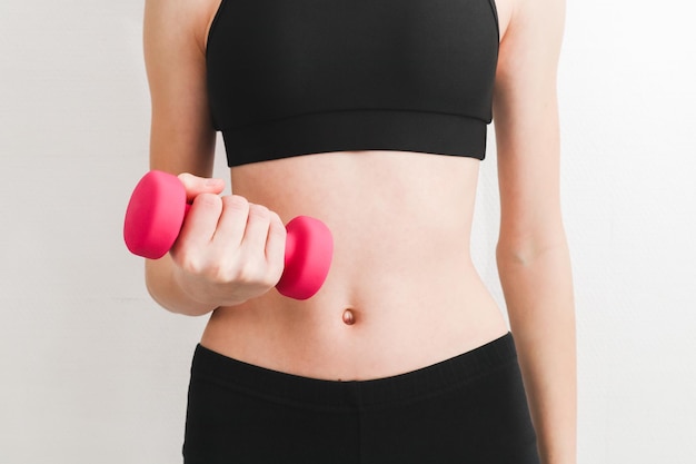 Young beautiful caucasian teen girl in a fitness suit holds pink dumbbell with one hand