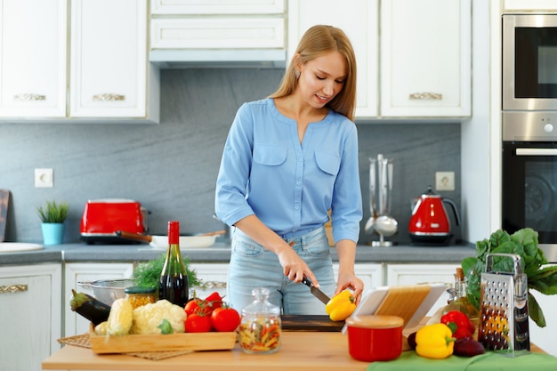 Young beautiful caucasian woman cooking and using her digital tablet in kitchen