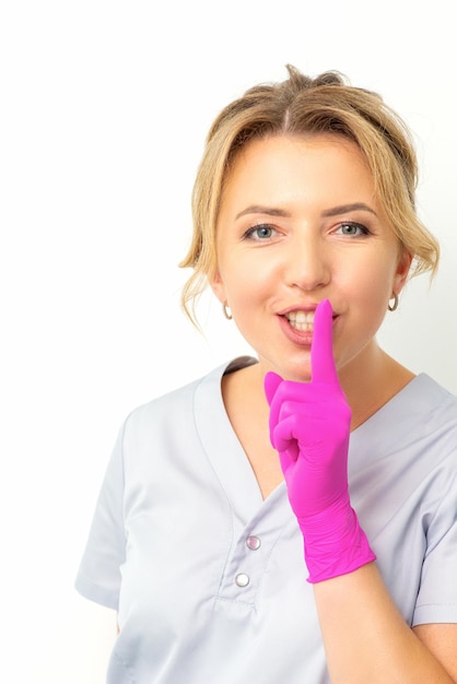 young beautiful caucasian woman doctor beautician doing silent gesture pressing his index finger to his lips isolated on white background
