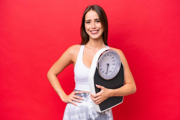 Young beautiful caucasian woman isolated on red background with weighing machine