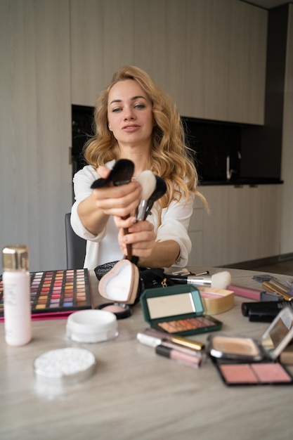 Фото Молодая красивая кавказская женщина, профессиональный блоггер или видеоблогер по красоте, пишет учебник по макияжу, чтобы поделиться им в социальных сетях. объясняет, как использовать кисти. концепция онлайн-обучения.