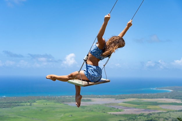 Young beautiful caucasian woman on the rope swing with sea and sky background concept of dream and happiness