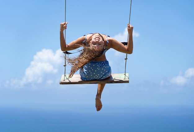 Young beautiful caucasian woman on the rope swing with sea and sky background. Concept of freedom and happiness.