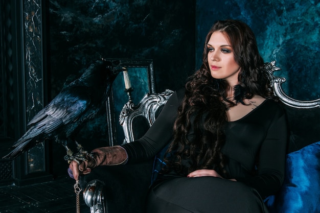 Молодая красивая кавказская женщина с черным вороном на руке сидит на диване