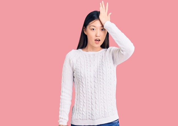 カジュアルなセーターを着た若い美しい中国人女性は、間違いを覚えて、悪い記憶の概念を忘れて頭に手を当てて驚いた