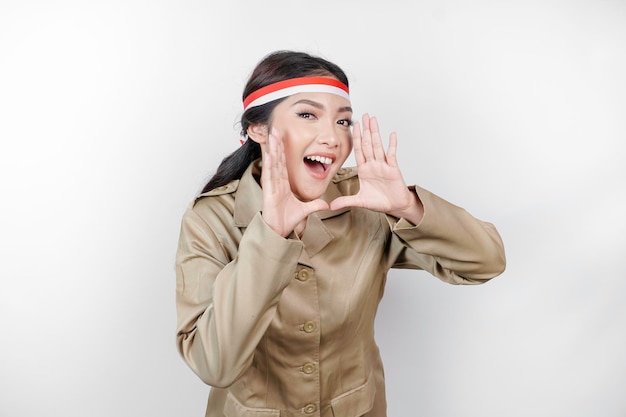 Young beautiful civil worker woman is wearing indonesia's flag headband and shouting or yelling isolated by a white background Communication and independence day concept