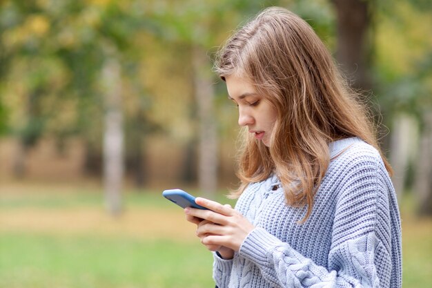 Young beautiful concentrated woman, teenager girl is looking at screen of her cell mobile phone