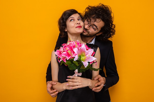 Young beautiful couple happy man and woman with bouquet of\
flowers smiling cheerfully embracing happy in love