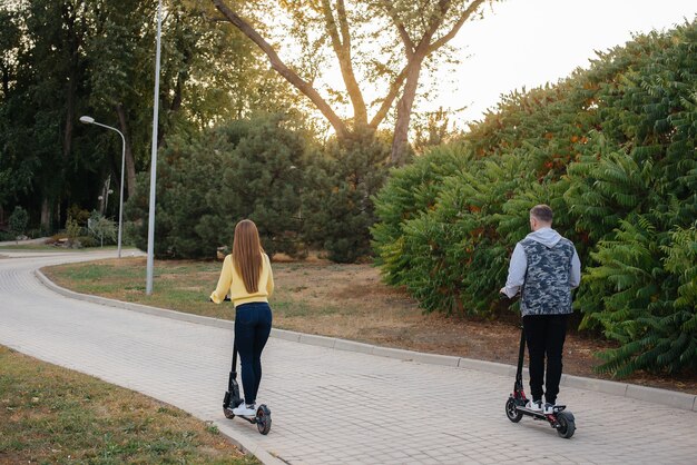 若い美しいカップルが暖かい秋の日に公園で電動スクーターに乗る