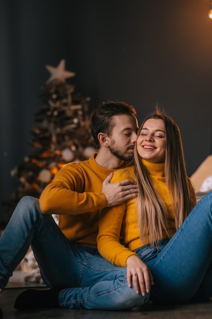 Young beautiful couple sitting on the bed against the background of the Christmas tree