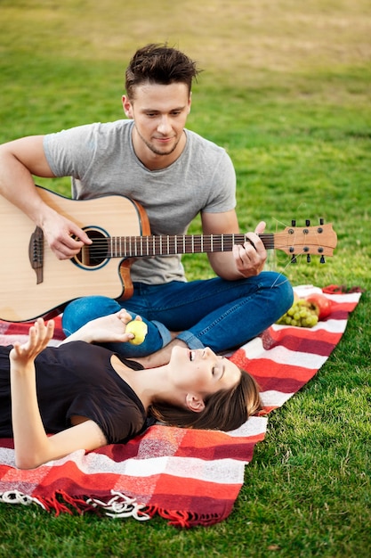 Giovane bella coppia sorridente che riposa sul picnic nel parco