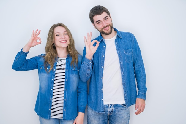 Young beautiful couple standing together over white isolated background smiling positive doing ok sign with hand and fingers Successful expression