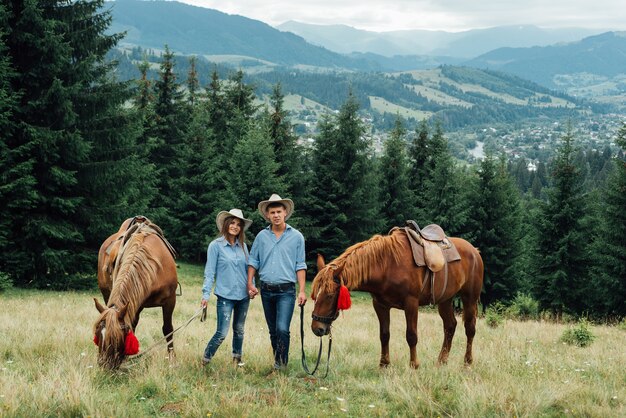 Young beautiful couple walk with horses in mountains