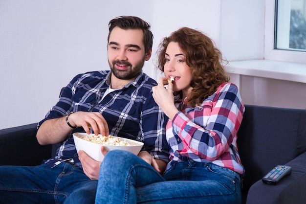 Young beautiful couple with popcorn watching movie on tv at\
home