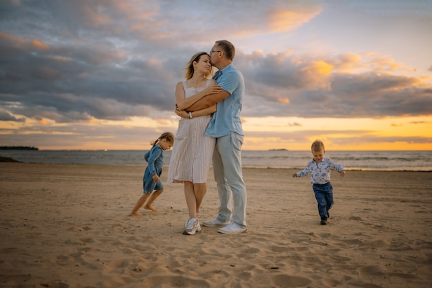 ビーチで走っている子供たちと若い美しいカップル背景の美しい夕日の空