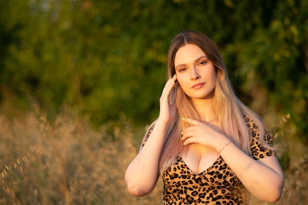 A young beautiful curvy woman in a leopard dress poses in a field at sunset