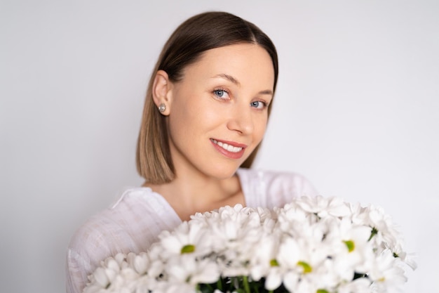 Foto giovane bella donna sorridente adorabile dolce carina con tenere un mazzo di fiori freschi bianchi su sfondo bianco muro