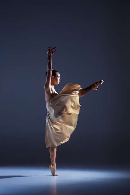 Young beautiful dancer in beige dress dancing on gray studio background