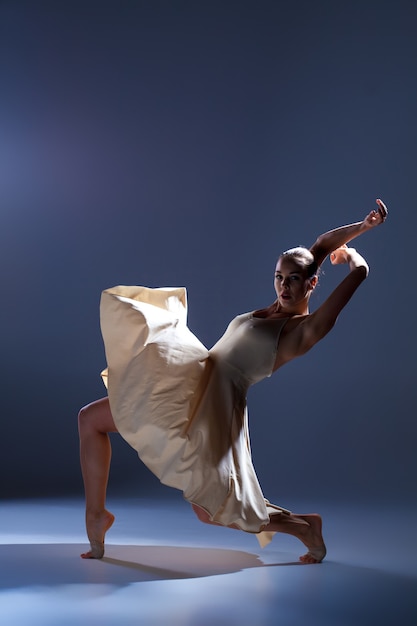 Молодая красивая танцовщица в бежевом платье танцует на сером студийном фоне