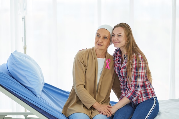 Foto giovane bella figlia si siede accanto alla madre che lotta per il cancro per sostenerla sul letto d'ospedale