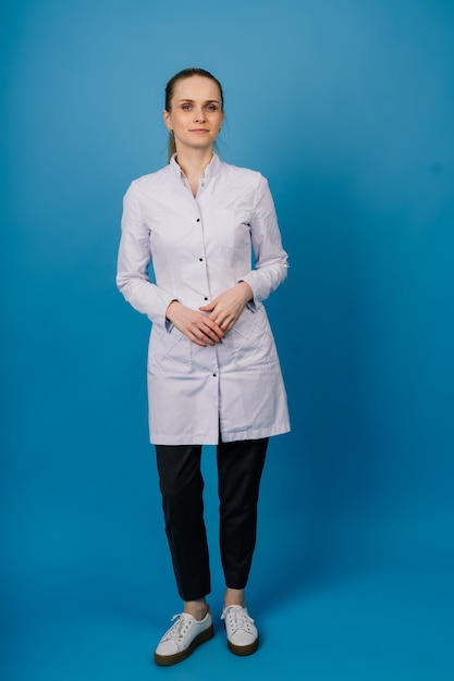 Young beautiful doctor woman in lab coat, studio shot, blue background