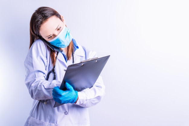 Giovane bella dottoressa che indossa abiti a due pezzi con una maschera che parla al telefono con un paziente che scrive un concetto di rapporto visita il concetto di medicina e tecnologia online del telefono medico