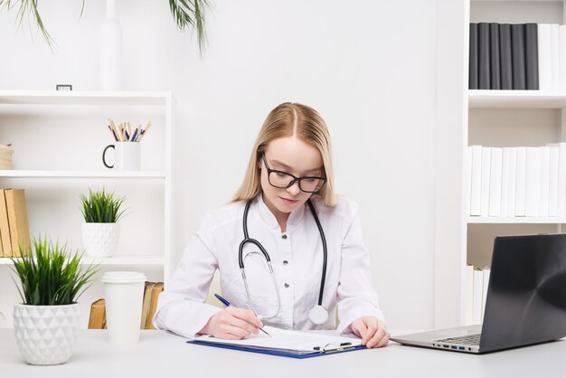 Young beautiful doctor woman working happy and smile in hospital, sitting on table, medical concept