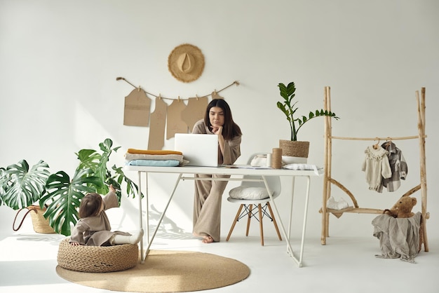 A young beautiful dressmaker making clothes at home Woman standing at table and working on a laptop