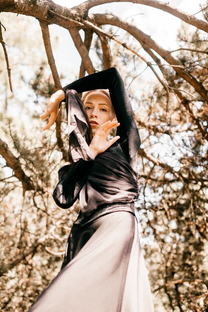 Young beautiful elegant woman in black vintage dress with veil posing among trees