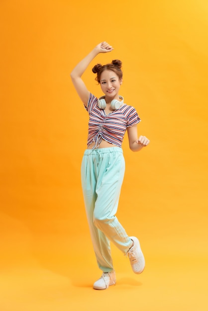 Young beautiful energy girl with white headphones listening to music laughs and jump on yellow background