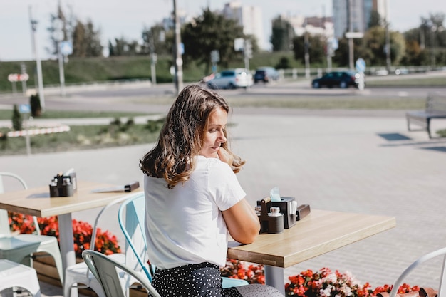 La giovane bella donna europea si siede in estate su una terrazza di un caffè?